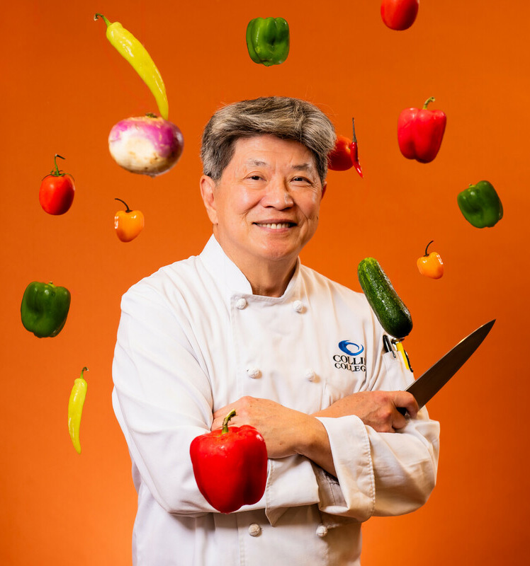 Nelson Wong stands in his chef's outfit surrounded by vegetables