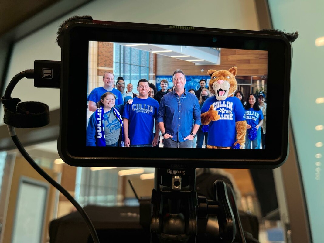 A group of people in Collin College gear are seen on a video camera viewing window.